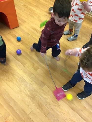 Several toddlers are hitting colourful balls with fly swatters.