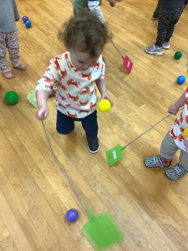 Several toddlers are using fly swatters to hit colourful balls.