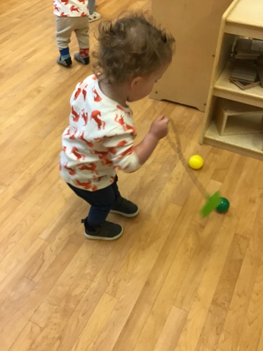 A toddler is using a fly swatter to hit some colourful balls.