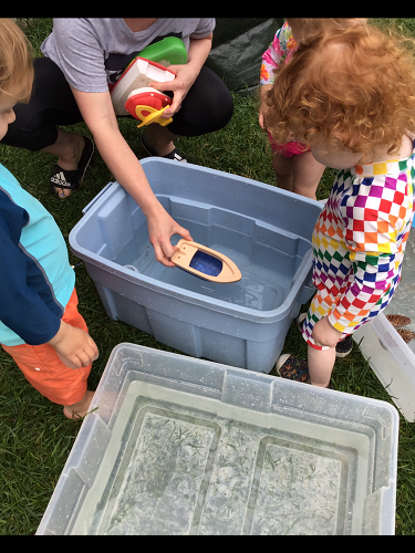 Toddlers are adding objects to buckets filled with water to see if they sink or float.