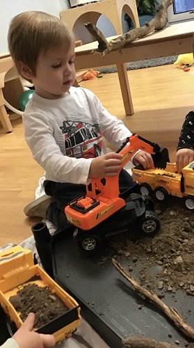 A toddler is driving two construction vehicles in the mud.