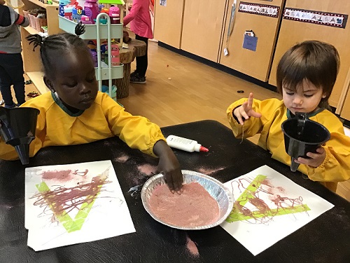 Two children adding sand to their art