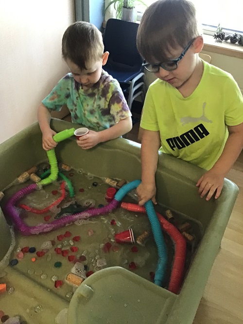 2 Preschool boys using tubes in sensory bin