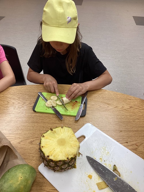 child using a knife to cut a piece of fruit