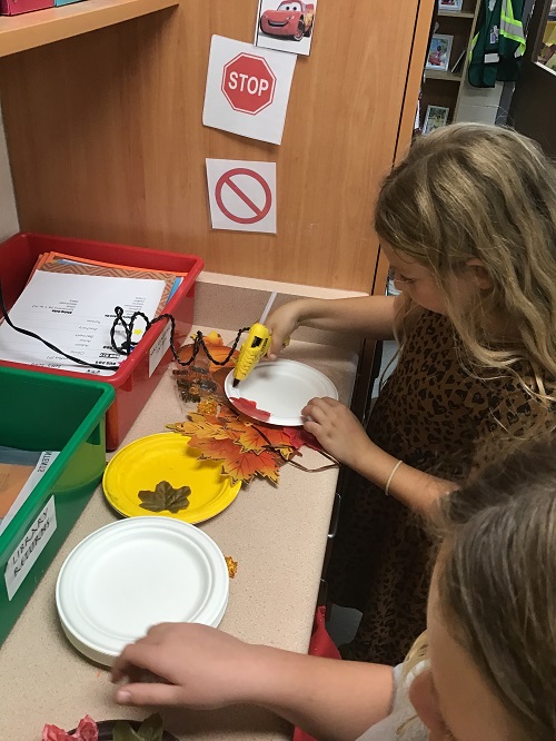 children using a hot glue gun to place leaves on a paper wreath