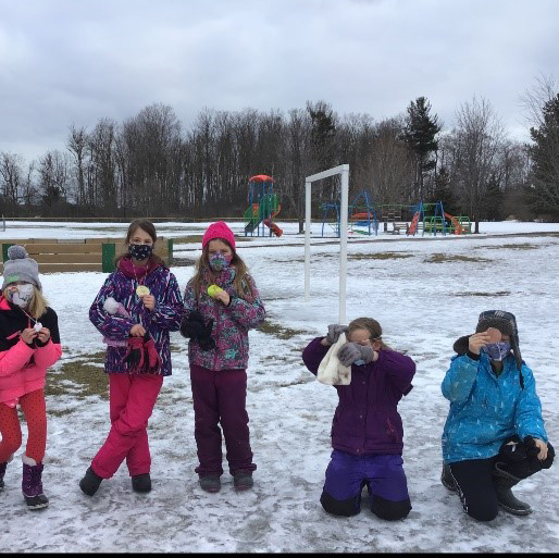 children standing and kneeling on ice in their snowsuits in the winter