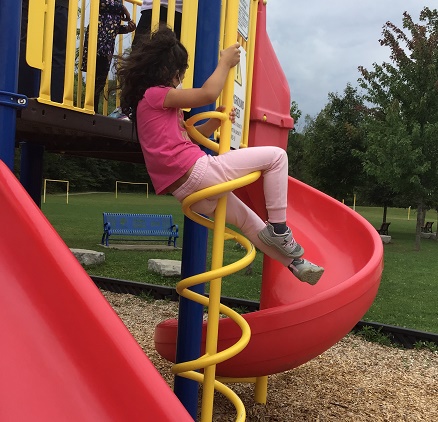 School age girl climbing down spirla pole on playground climber
