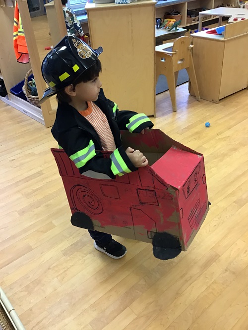 Child pretending to ride his cardboard fire truck.