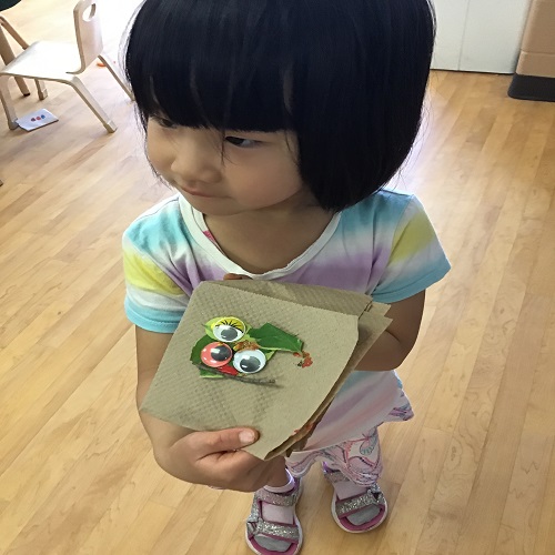 Child showing their created bug out of leaves and googly eyes. 