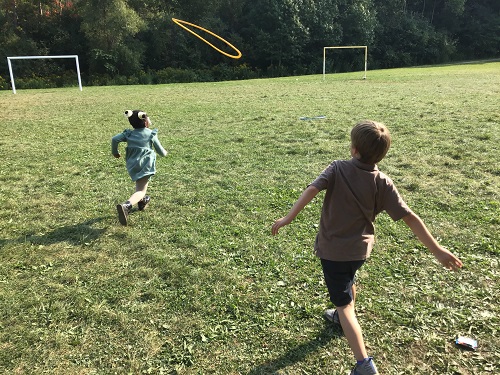 Children running after a hula hoop.