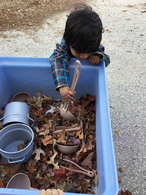 Child scooping leaves with a ladle.