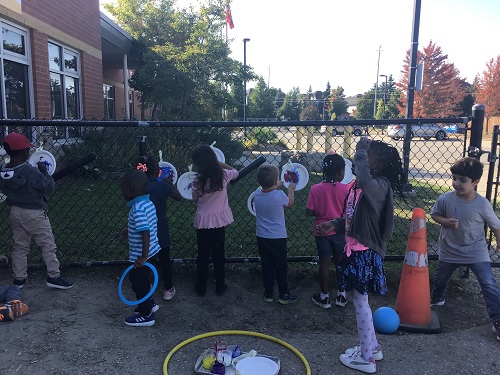 Children painting on paper plates on the fence. 
