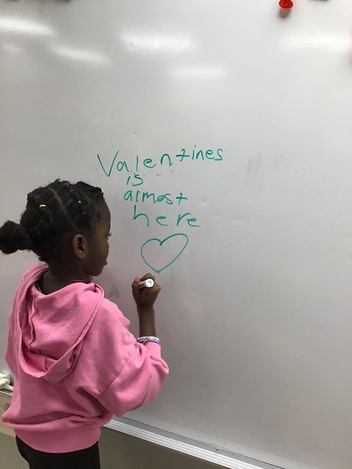 Child writing Valentine's message on the whiteboard.
