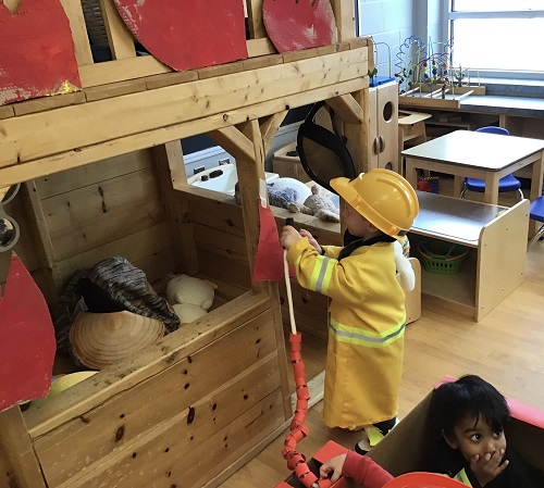 Another child takes a turn to put the fire out with the hose and firefighter uniform on.