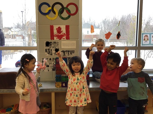 Group of children sitting by the Olympic rings, cheering.