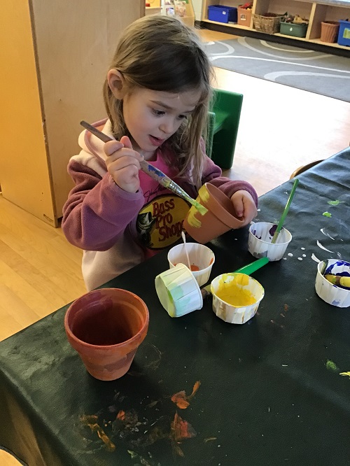 Child painting a terracotta flower pot.
