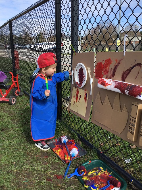 Child painting on a paper plate on the outdoor fence.