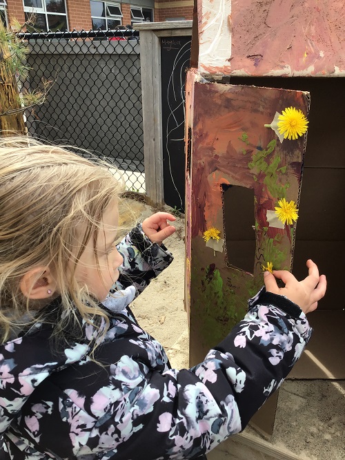 Child adding dandelions to their painted cardboard box.