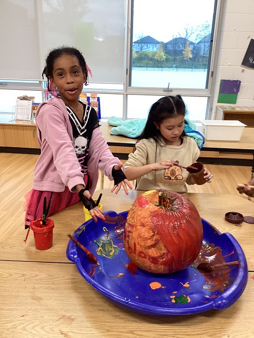 2 school age girls decorating a pumpkin