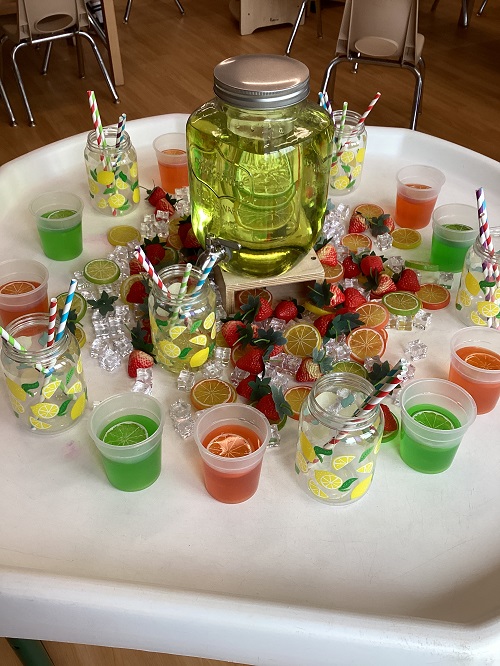 A tuff tray set up using colourful water, cut limes and oranges, and cups