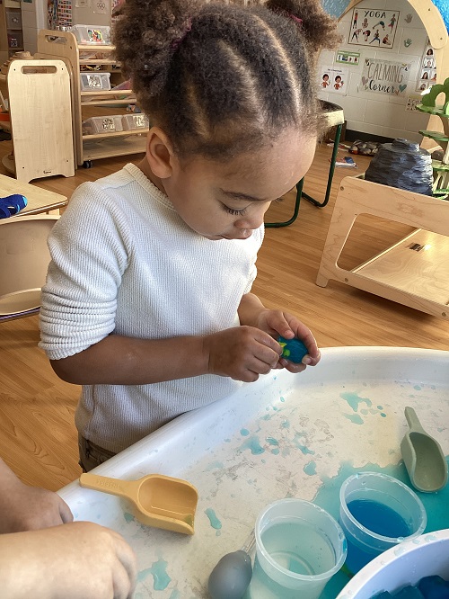 A preschool child trying to free a toy duck from a frozen ice cube