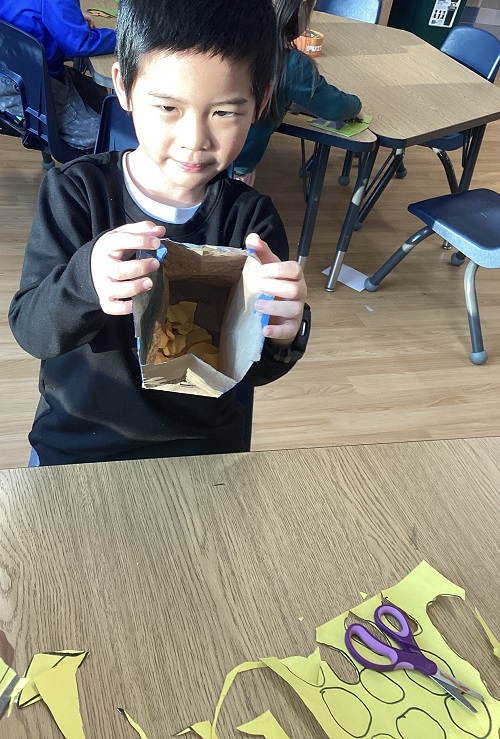 A school age child holding a bag with cut up shapes inside