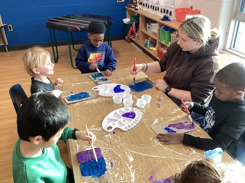 A group of school age children sitting at a table painting their chip bags