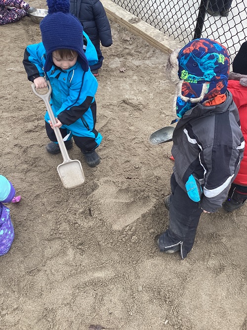 Children in the sand box working collaboratively to dig a hole