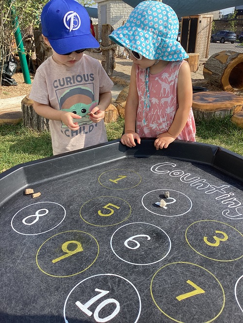 Two children looking at an item to add to their tuff tray scavenger hunt.