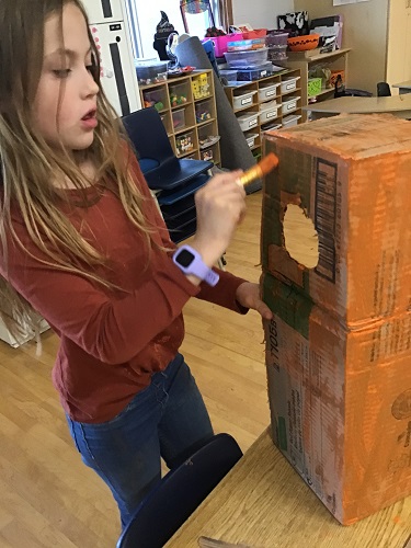school age girl painted a box with orange paint to create a pumpkin costume 