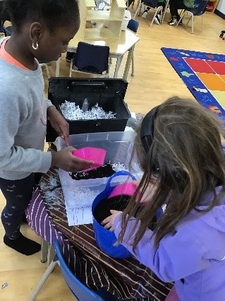 2 school age children filling bins with dirt and shredded paper 