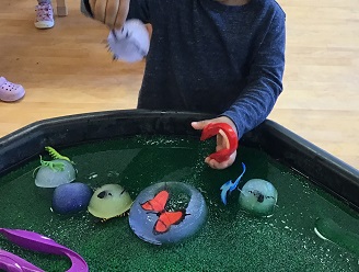 image of child's hands manipulating tongs and insects encased in ice