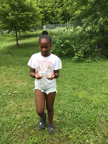 school age girl holding two clear orbs while walking across grass 