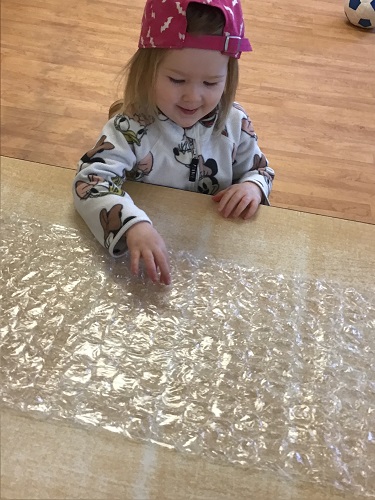 toddler child popping bubbles on large bubble wrap 
