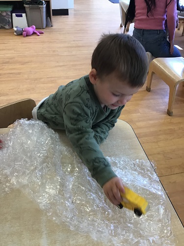 toddler child rolling a toy car across bubble wrap.  Popping the bubbles. 