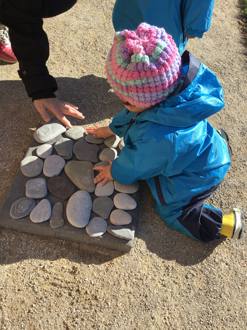 child learning on a block of scattered stones outside