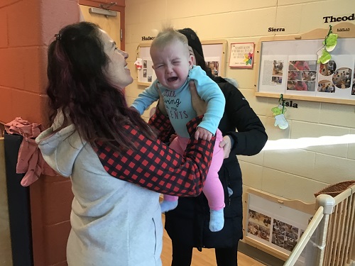 Parent passing crying infant to their educator for hugs