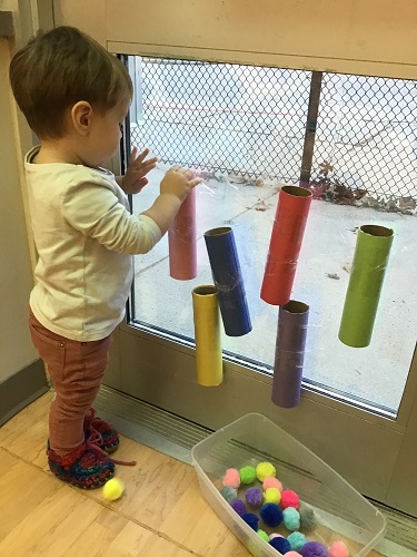 An infant dropping pom poms into tubes