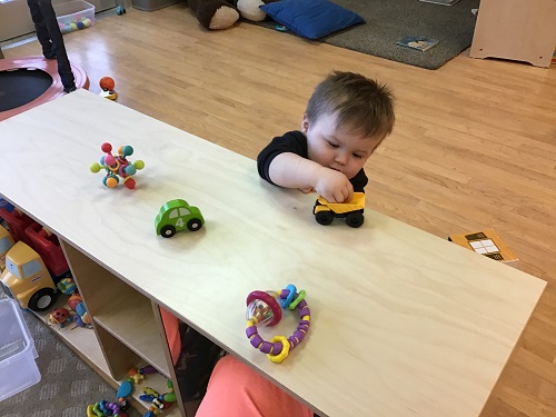 An infant driving cars on the shelf top