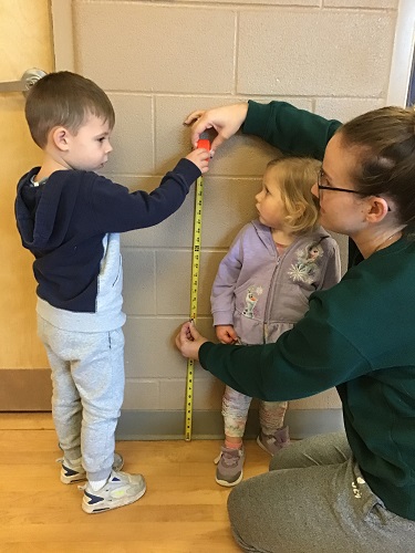 Educator and child using a measuring tape to see how tall another child is