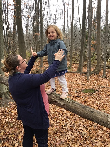 Educator supporting a child as they stand on a fallen tree