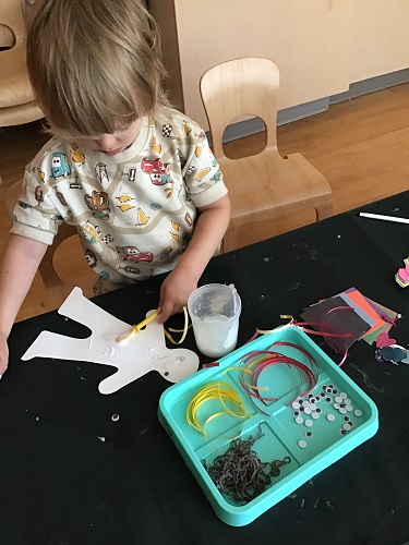 A child spreading glue on their paper person
