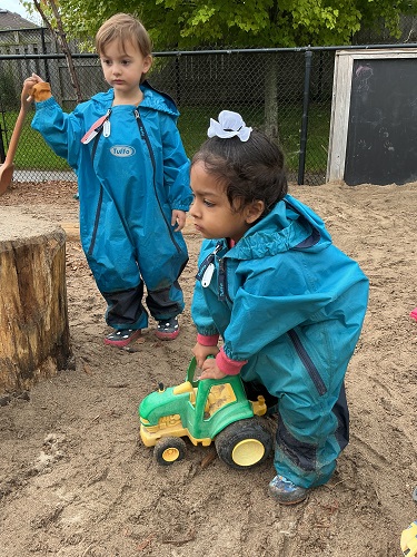 Preschool child pushing a toy tractor through the sand