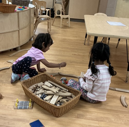 Two preschool children building with train tracks