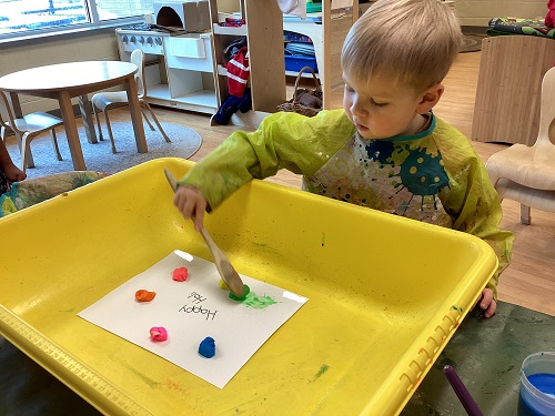 A child using a wooden spoon to create colour splats on paper