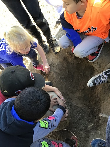 School age children moving a big rock from the ground