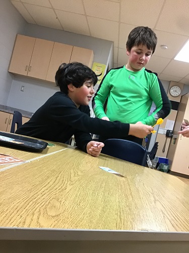 A school age child passing a dart to a peer to try and win their groceries by playing a game.