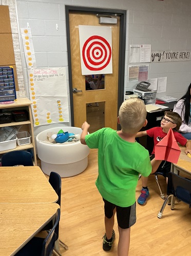 school aged child getting ready to throw paper airplane at bullseye