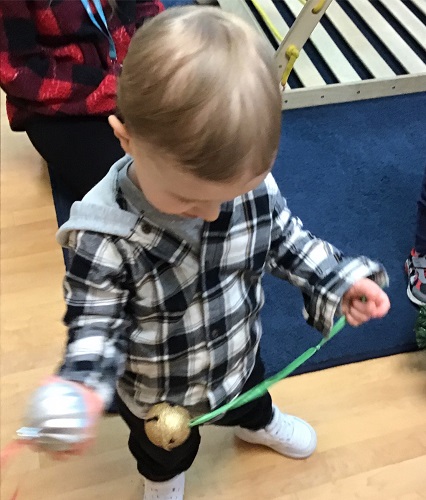 Toddler looking at a bell on a ribbon