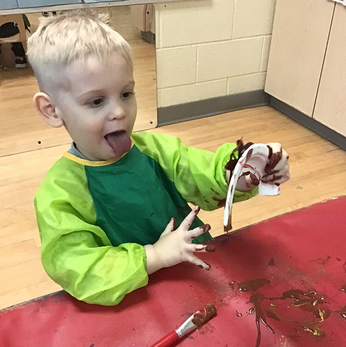 A toddler sticking his toung out as he looks at what he just painted